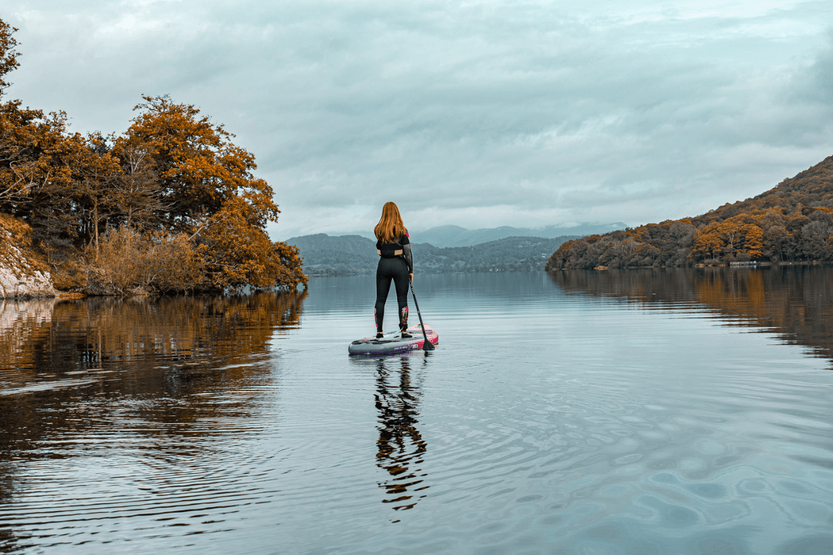 Mujer practicando paddle surf en un lago otoñal