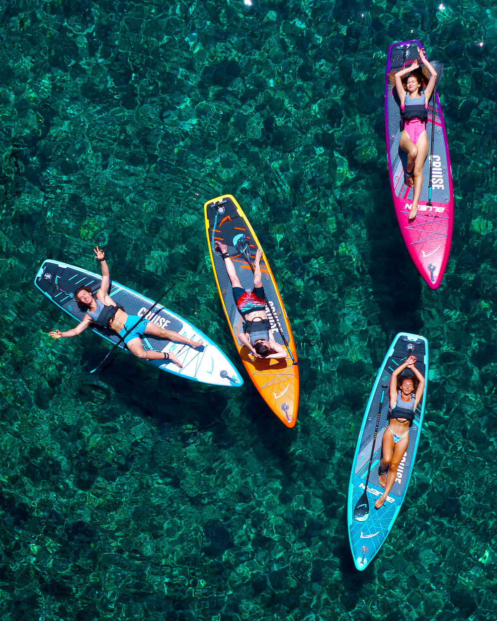 Four paddleboarders relaxing on colorful inflatable paddleboards in clear water