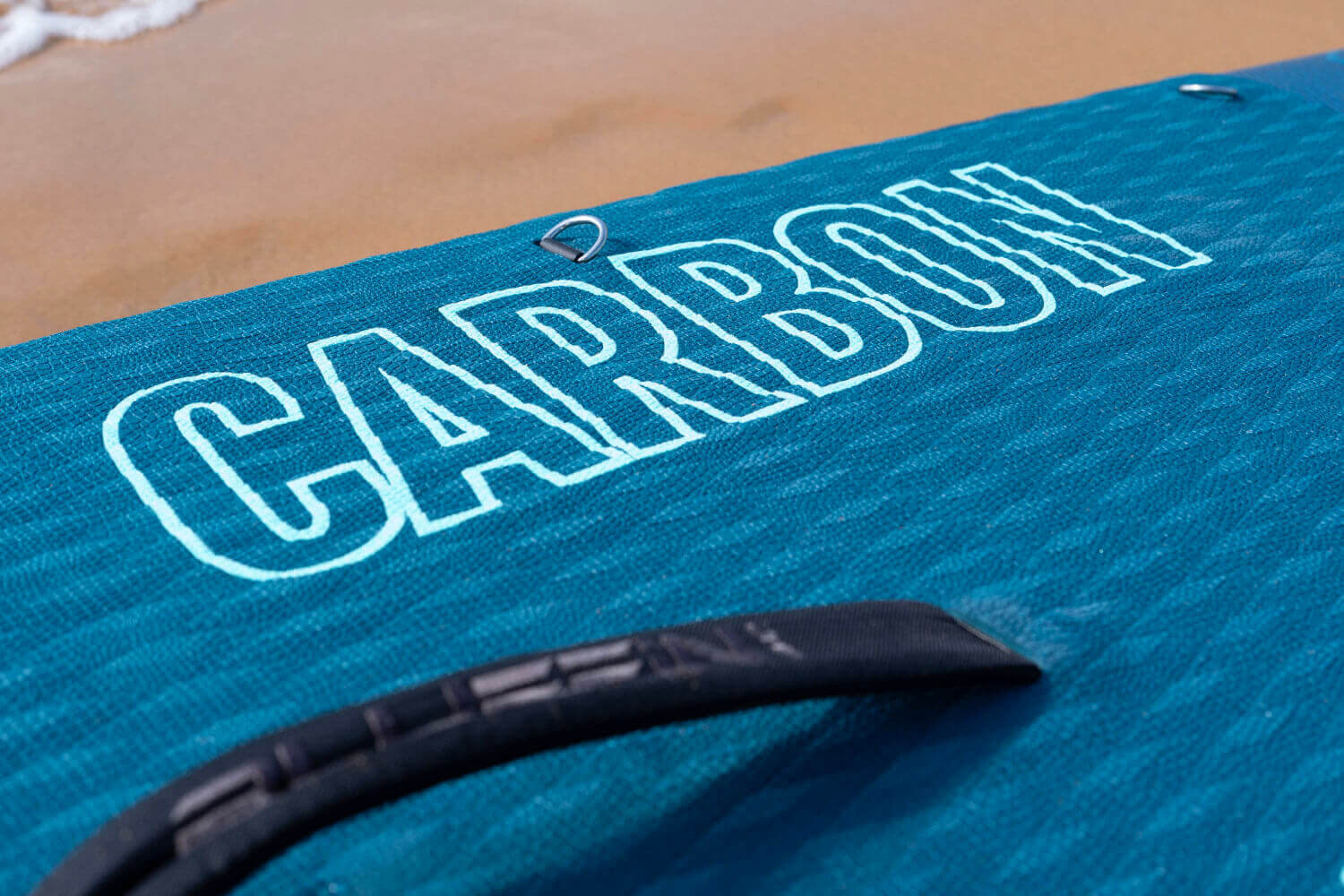 Teal inflatable paddleboard with the word 'CARBON' printed on the deck and a black handle