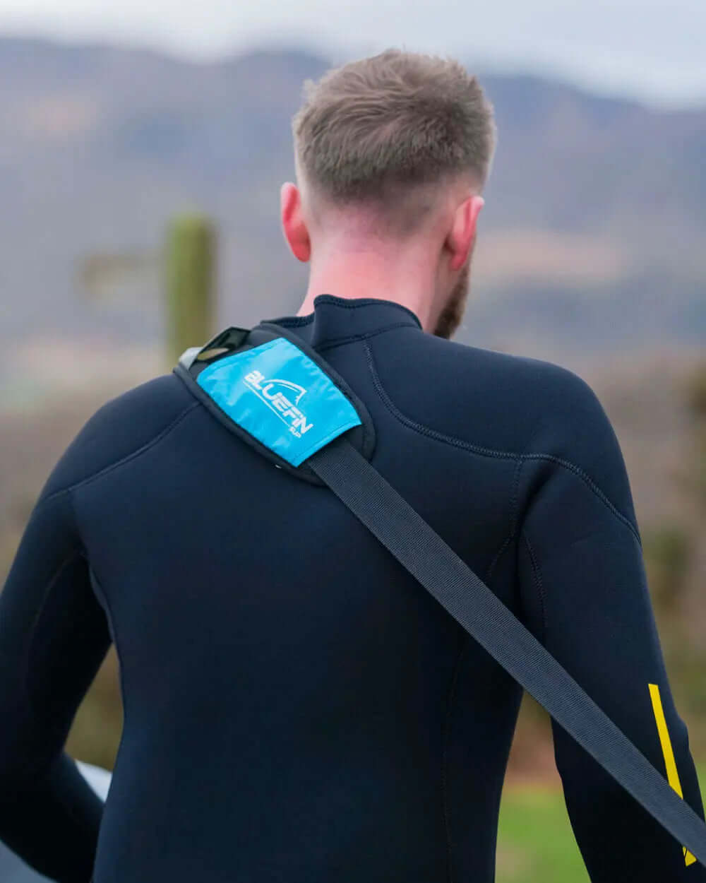 Person wearing a black wetsuit with a blue Bluefin bag slung over their shoulder outdoors