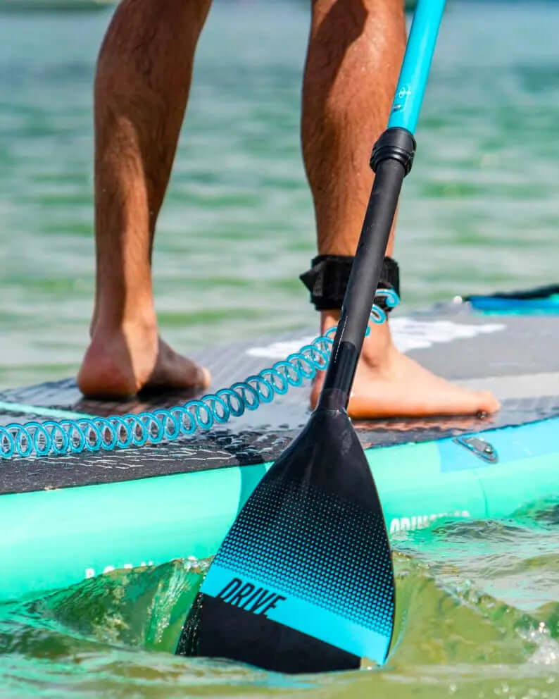 Persoon op een paddleboard met een zwarte peddel met blauwe accenten, water spettert rond de peddel