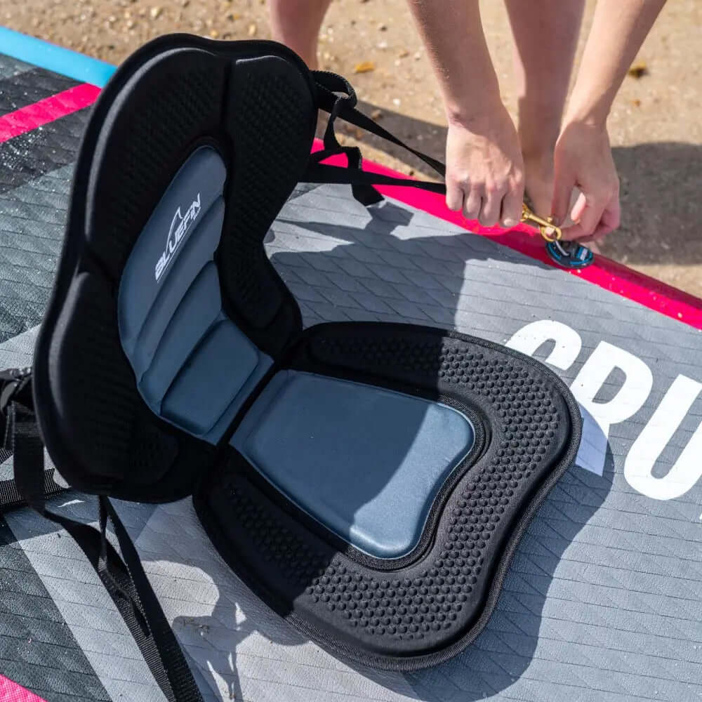 Black and gray padded seat on a paddleboard with a person securing a strap.