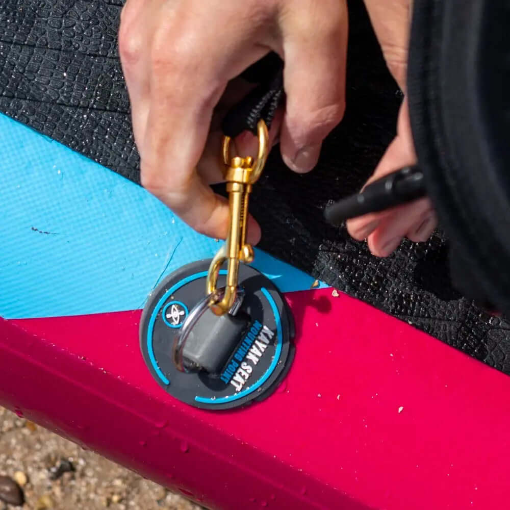 Hand attaching a golden clip to the inflation valve of a colorful inflatable paddleboard