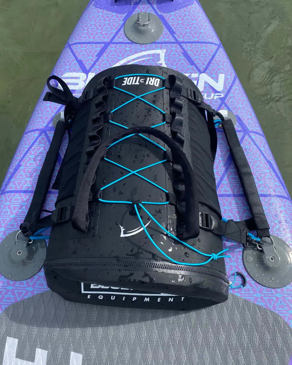 Black dry bag with blue straps and laces on a purple paddleboard with textured surface