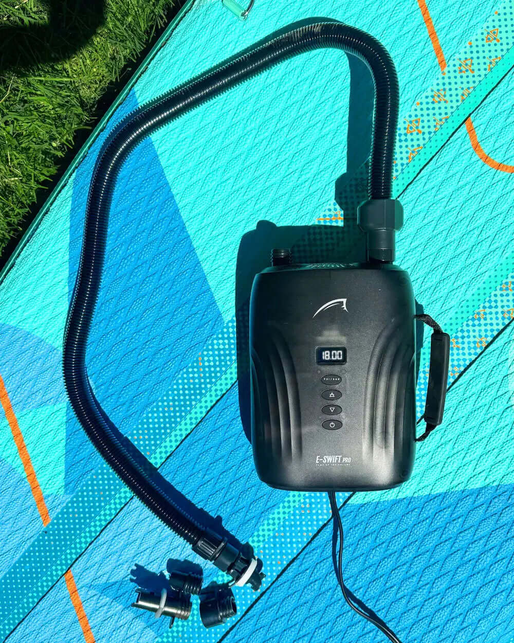 Black electric pump with digital display and hose, next to connectors on a blue textured surface