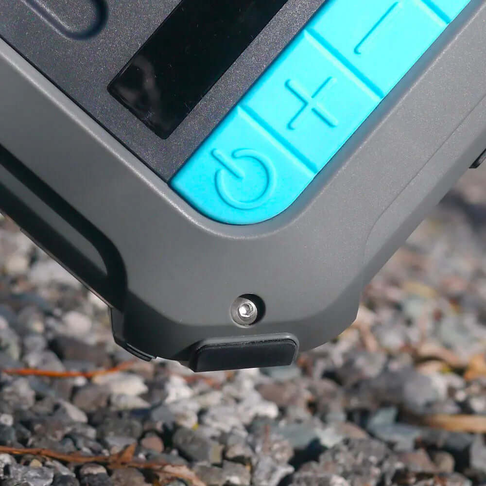 Close-up of a gray device with blue buttons, power button, and a small silver screw on a rocky surface.