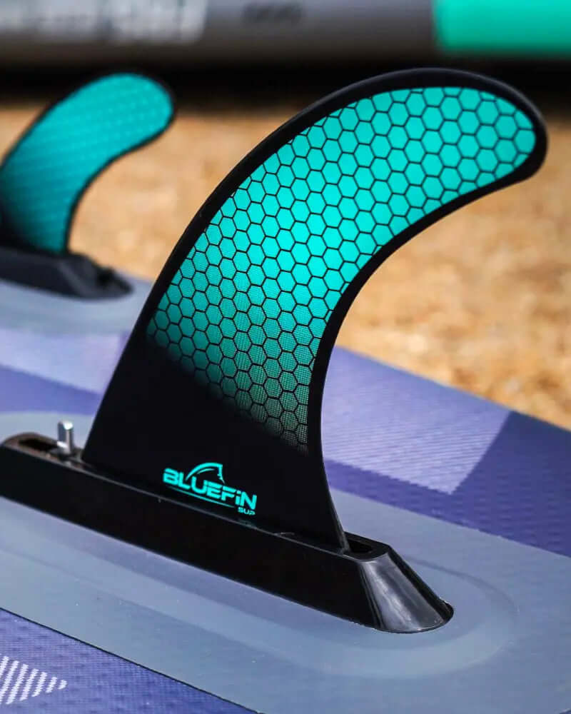 Close-up van een paddleboard vin met een honingraatpatroon en het BLUEFIN-logo op een gestructureerd oppervlak
