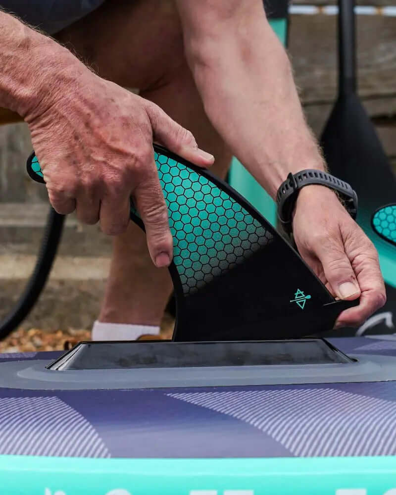 Persoon bevestigt een zwarte vin aan een opblaasbare paddleboard met een gestructureerd oppervlak
