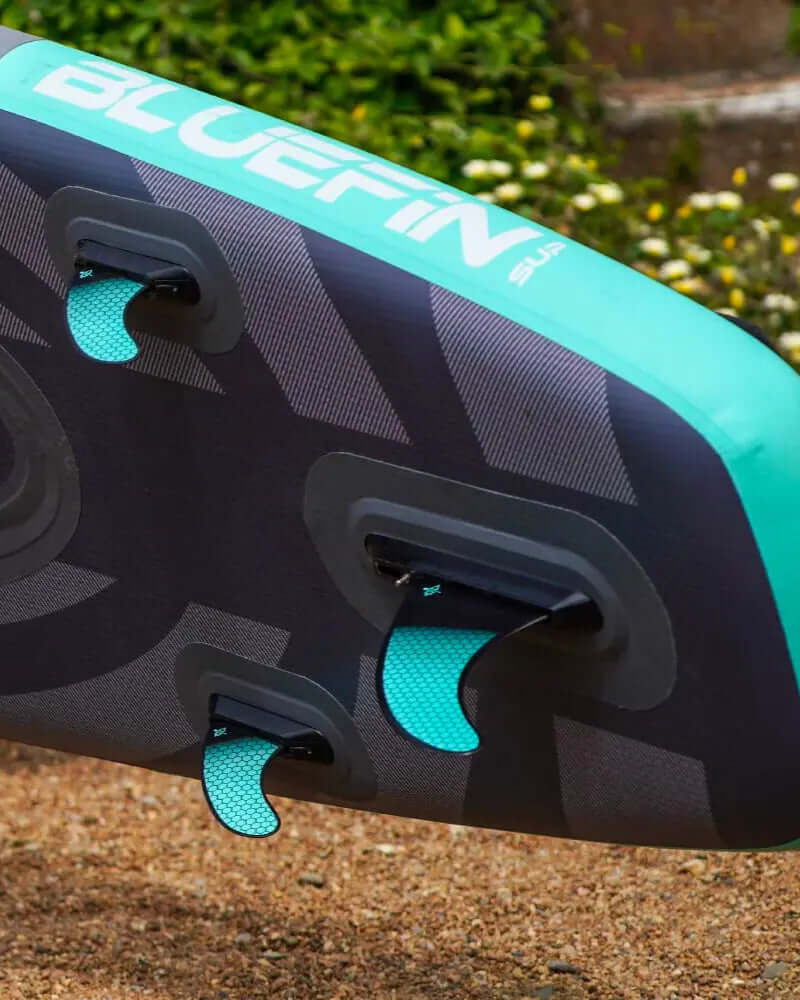 Opblaasbare paddleboard met twee vinnen, gestructureerd oppervlak en branding in teal en zwarte kleuren