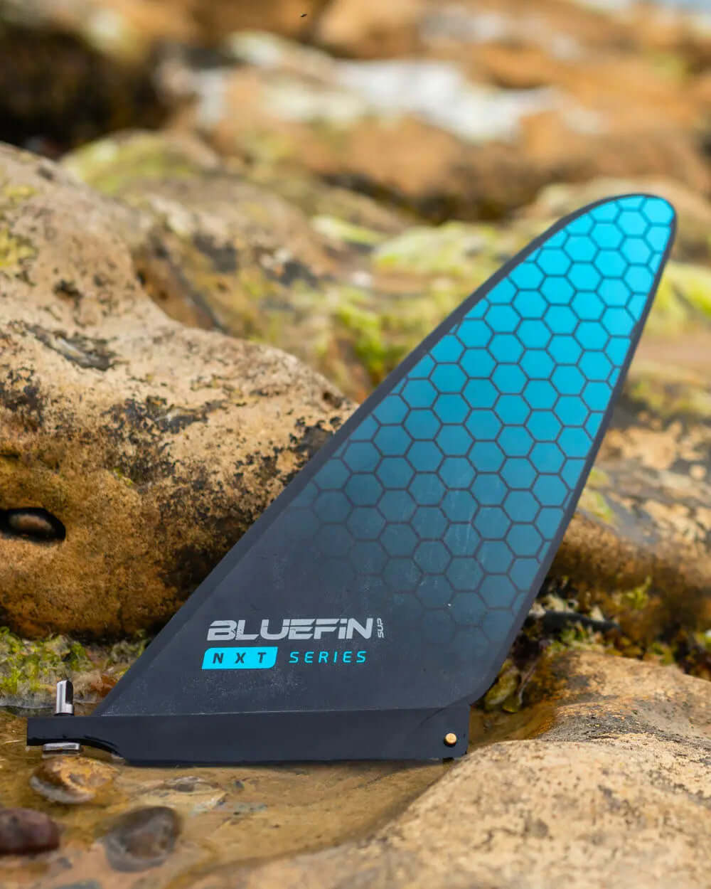Bluefin NXT Series fin with a hexagonal pattern, resting on rocky terrain near water.