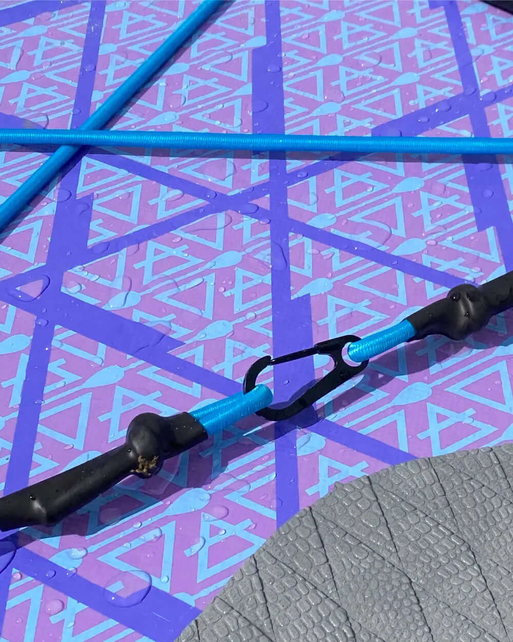 Close-up of a blue bungee cord with black clips on a textured purple paddleboard surface