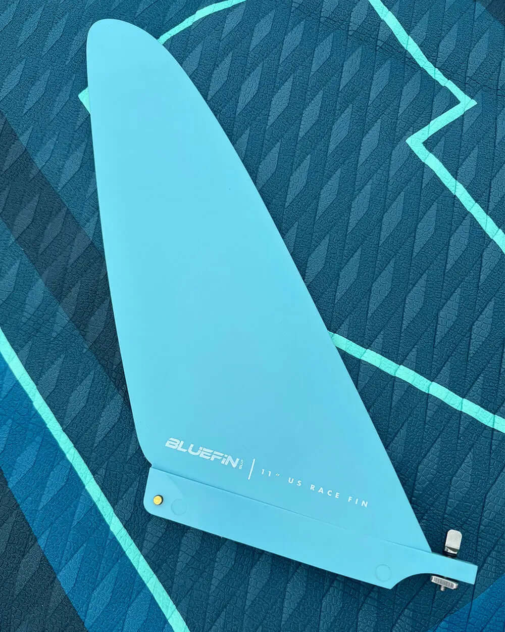 Light blue 11" US race fin on a textured dark blue paddleboard surface