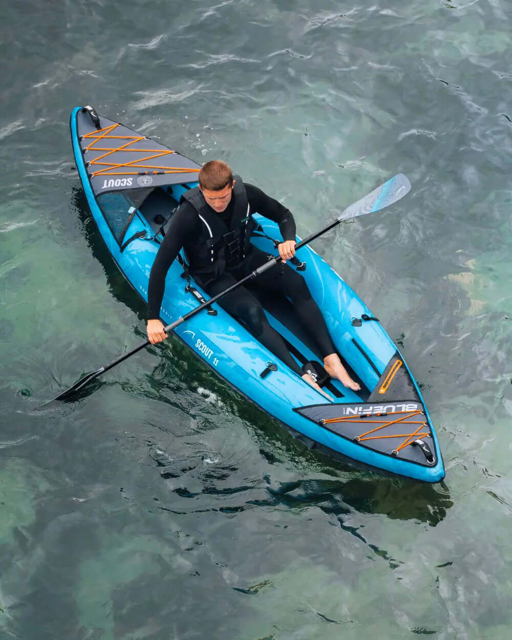Person paddling a blue inflatable kayak on clear water, wearing a black wetsuit and life jacket.