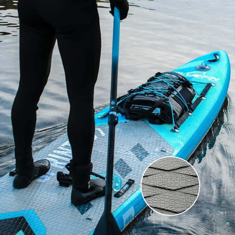Paddleboard mit strukturiertem Deckpad, schwarzer Rucksack gesichert, Person hält Paddel im Wasser