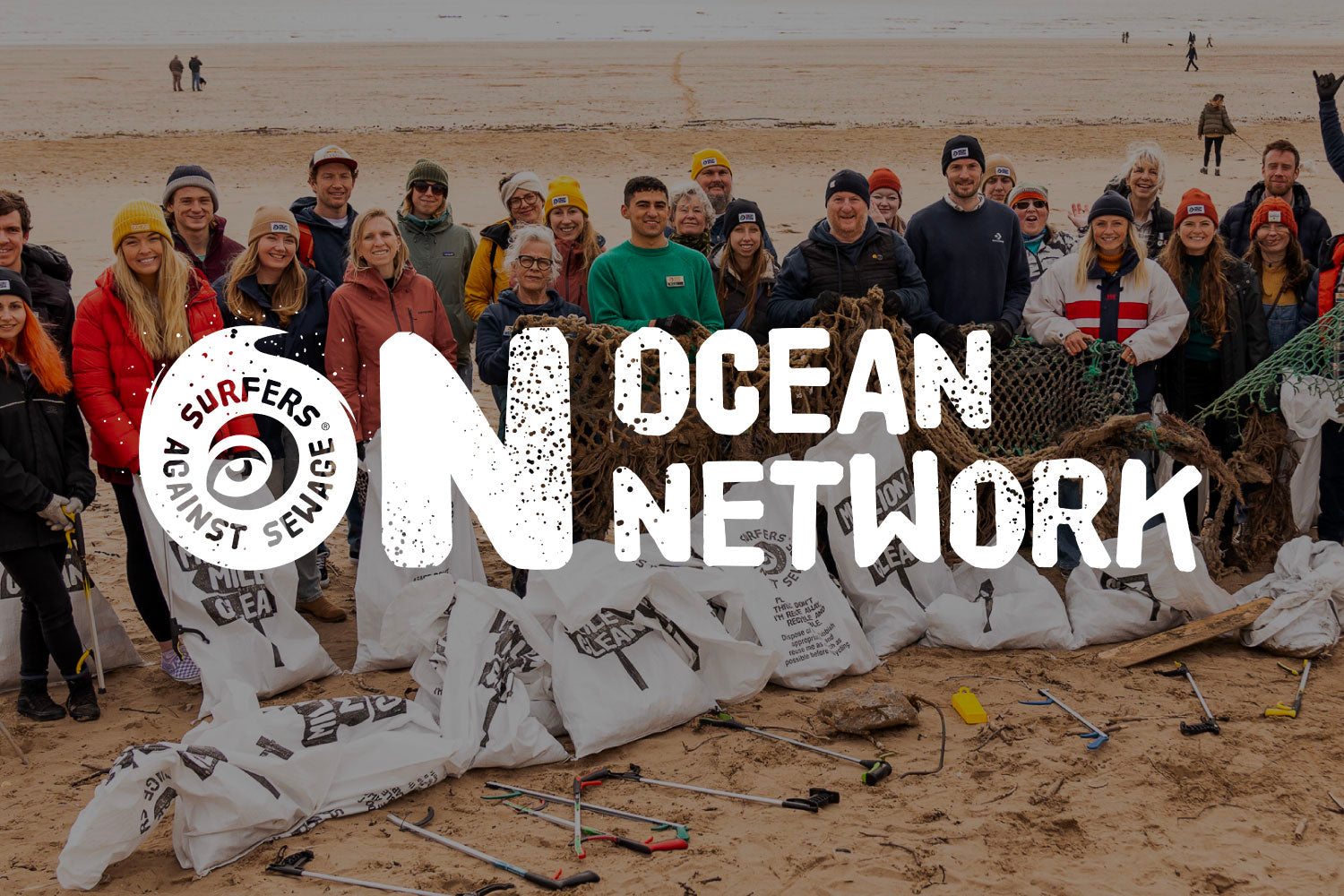 Group of volunteers on a beach holding trash bags and nets for an ocean cleanup event
