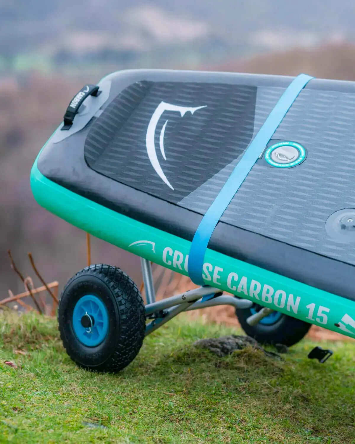 Opblaasbare paddleboard met een textuur op het dek, blauwe riem en wielen voor gemakkelijke transport op gras.