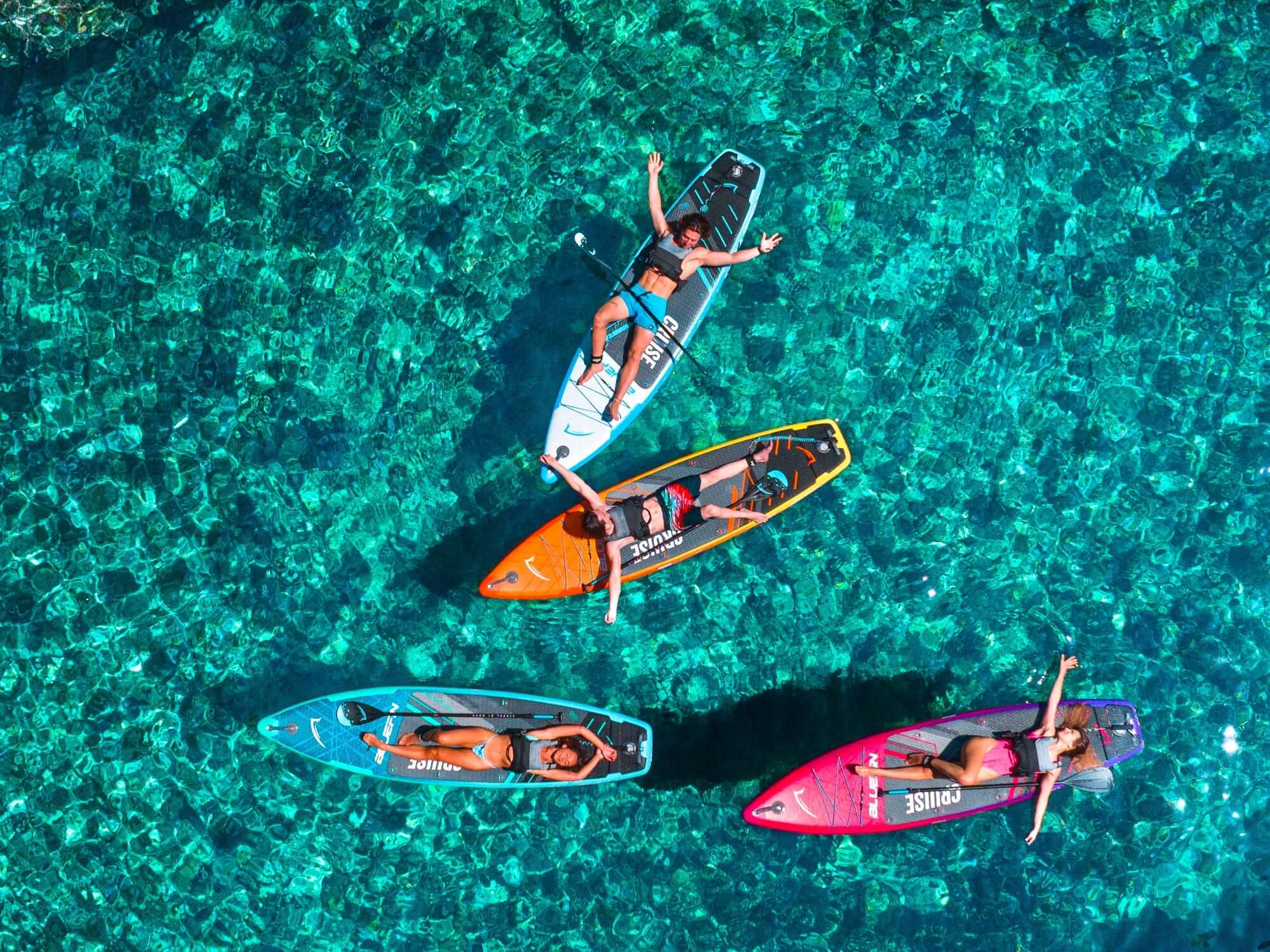Vier paddleboarders die ontspannen op kleurrijke boards boven helder turquoise water.