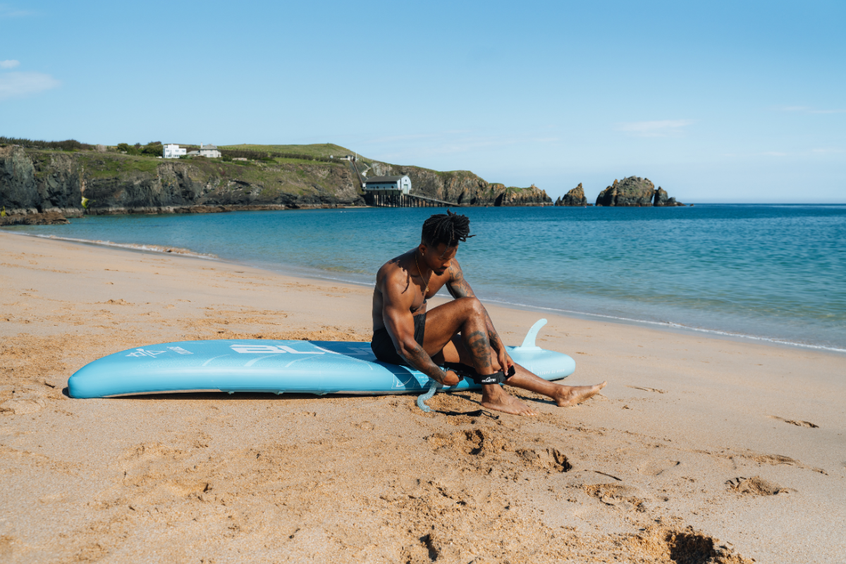 Man sat on paddleboard doing up his ankle leash