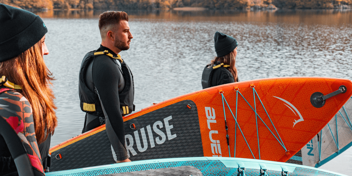 three people holding paddleboards, ready to head out onto the water