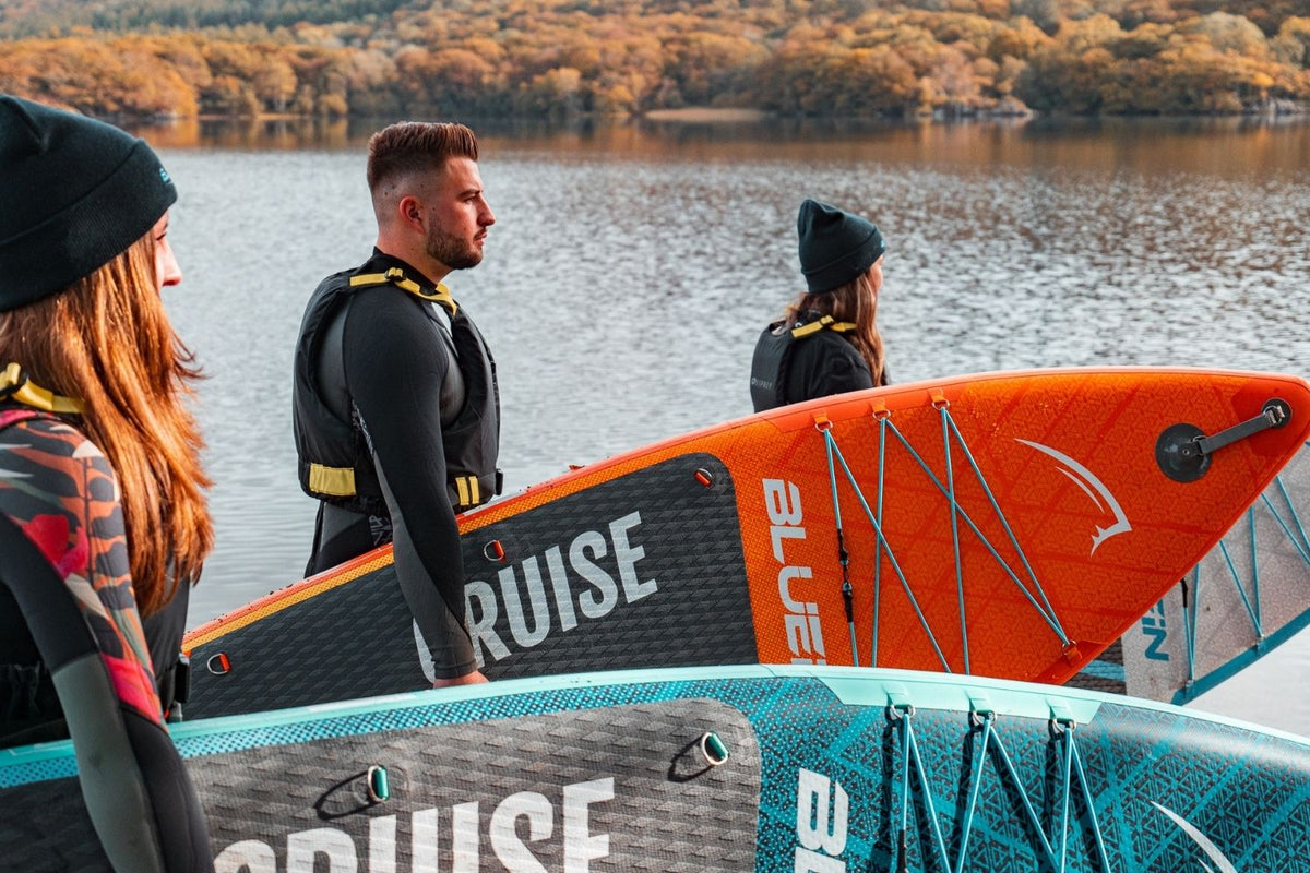 three people holding paddleboards by the edge of an autumnal lake