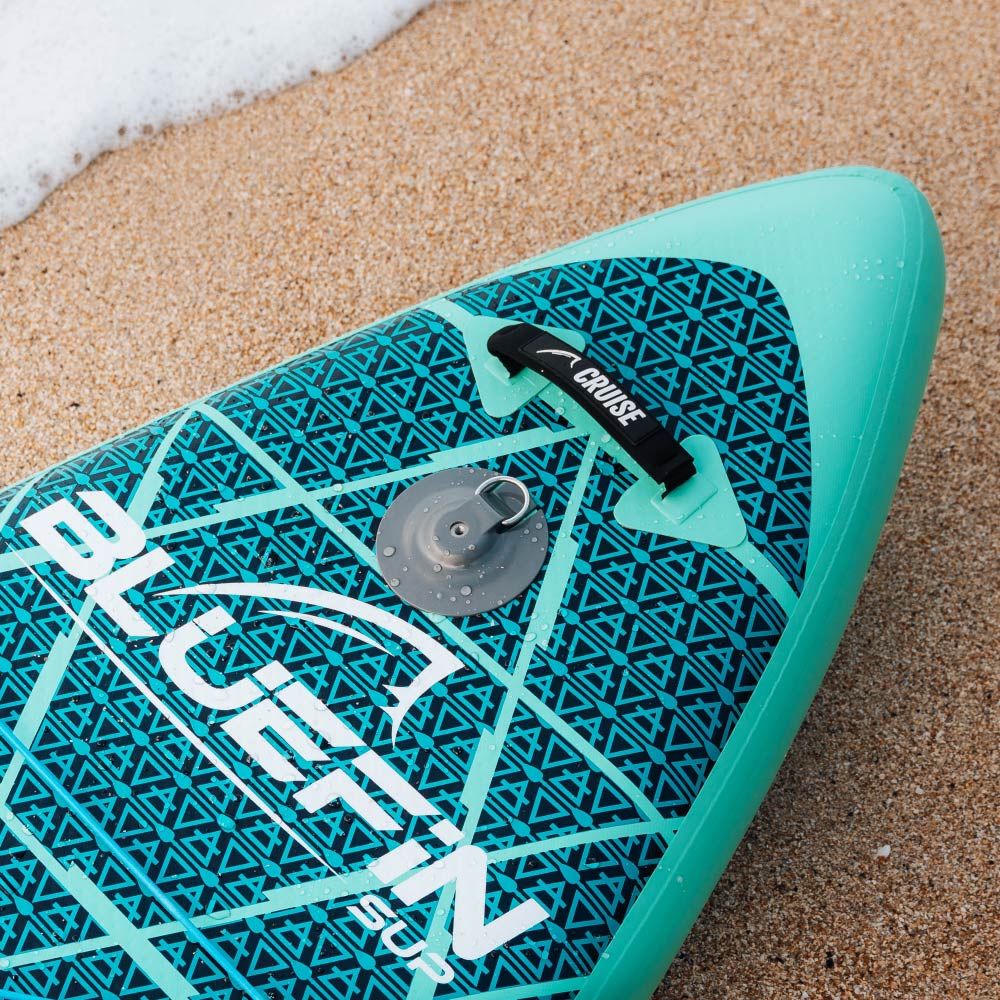 Inflatable paddleboard with turquoise design, center fin, and inflation valve on sandy beach