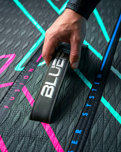 Hand gripping a textured strap labeled 'BLUEFIN' on a paddleboard with colorful graphics