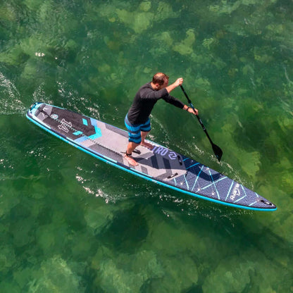 Homme pagayant sur une planche à pagaie gonflable bleu et noir au-dessus d'une eau verte claire