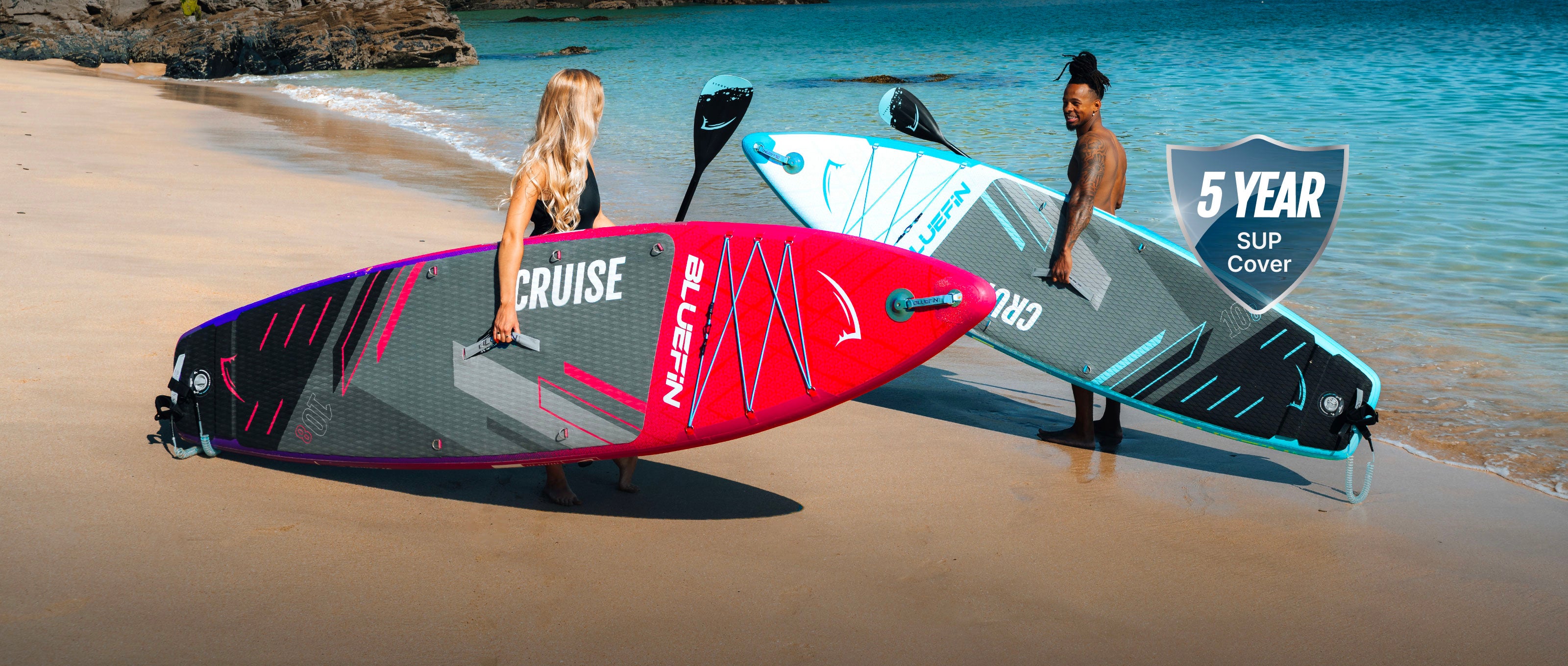 Two inflatable paddleboards on a beach, one pink and one blue, with riders holding them.