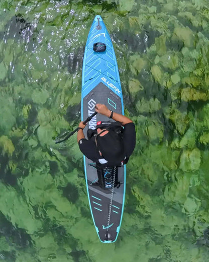 Person paddling a blue inflatable paddleboard over clear green water with visible rocks below